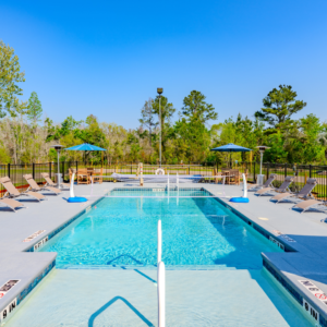 Wide shot of the outdoor pool at Lake City RV Resort, there is a net over the middle of the pool for volleyball. The pool is surrounded by lounging chairs and two umbrellas in the far corners. The pool is gated.