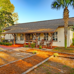 Exterior of Clubhouse building, tan with brown shingle roof, and 3 red rocking chairs on the front porch