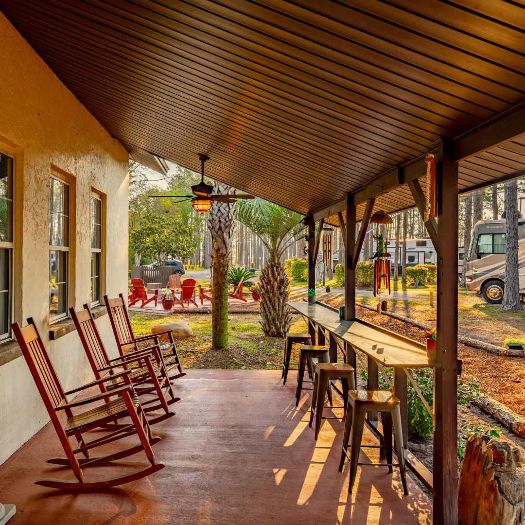 Exterior shot of the Lake City Resort clubhouse, the front porch has wooden rocking chairs and a small wooden bar with four metal stools behind it.