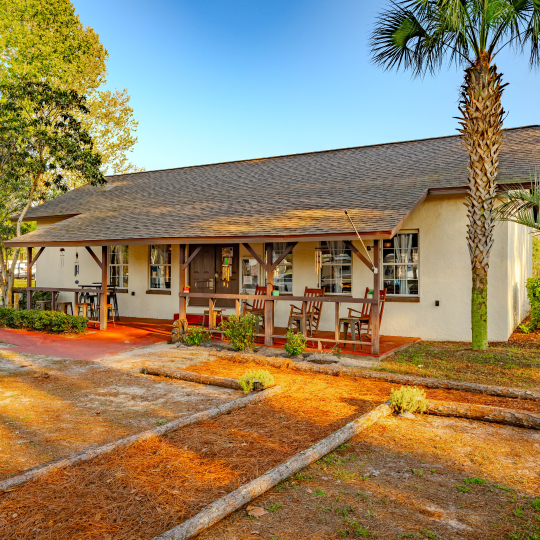 Exterior of Clubhouse building, tan with brown shingle roof, and 3 red rocking chairs on the front porch